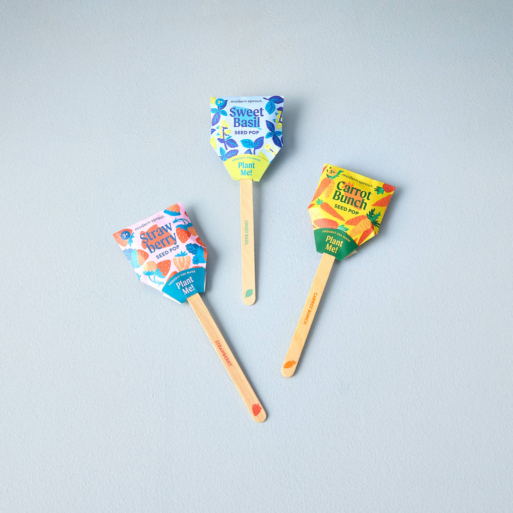 Three Garden Seed Pops (Single)—labeled "Strawberry," "Sweet Basil," and "Carrot Bunch"—rest on a light gray surface. Each features a colorful, family-friendly design with a wooden stick marked "Plant Me!"—ideal as a vegetable garden starter.