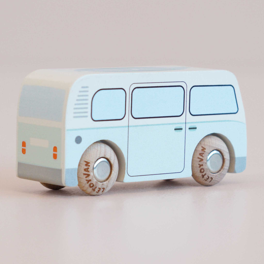 A No. 29 GT160 Daisy campervan toy, made in England, featuring a light blue vintage wooden design with simple painted details and rounded wooden wheels, displayed on a plain light surface. Its retro style evokes slow adventures and timeless play.