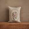 The Coral & Tusk Sugar Egg Pocket Pillow features embroidered florals and animals in an oval frame, creating a charming Easter accent on a rustic wooden surface against a textured beige wall.