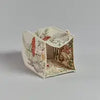 A small, decorative paper theater featuring intricate printed designs, set against a plain gray background. Its three-dimensional form suggests a miniature stage setting with Coral & Tusk Mushrooms and Ferns Tissue Box Covers.