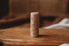 The Flower Roller - Eco Pattern Playdough Roller, a cylindrical wooden stamp with intricate floral carvings, stands upright on a wooden surface against a soft brown backdrop—an ideal eco-friendly tool for sensory play and creative playdough activities.