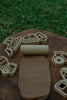 Toy construction vehicle-shaped cookie cutters and the Road Roller - Eco Pattern Playdough Roller are arranged on a board, with grass in the background. The eco-friendly Road Roller has imprinted a winding road pattern onto brown dough, making it perfect as a sensory play tool and for inspiring imaginative fun.