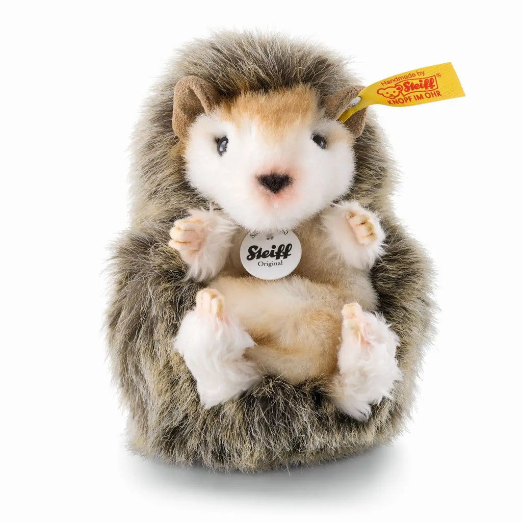 The Steiff Joggi Baby Hedgehog Stuffed Plush Toy, 4 inches, features soft brown and white fur, tiny paws, a black nose, Steiff’s yellow ear tag, and sits upright with the Steiff Original label on its chest.