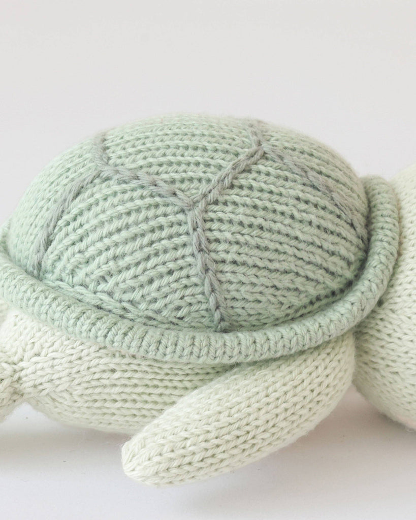 A close-up of the Cuddle + Kind Baby Sea Turtle (Kelp Green), showcasing its hand-knit textured shell and soft flippers against a plain white background—an adorable, heirloom-quality toy.
