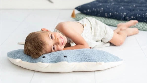 A young child lies on a Light Blue Stingray pillow on the floor, smiling at the camera, with a blue blanket in the background.