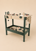 The Konges Sloejd Tool Bench is a charming wooden toy workbench featuring realistic tools and accessories—including a saw, hammer, wrench, and bolts—crafted in natural wood and dark green hues. Set against a beige background, this kids workbench is perfect for inspiring imaginative play with authentic wooden tools.