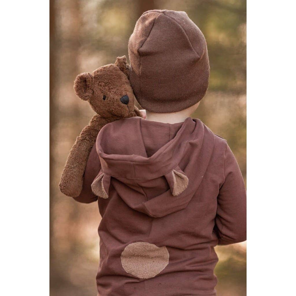 A young child, seen from behind outdoors, wears a brown bear-ear hoodie and holds the Senger Naturwelt Stuffed Animal - Large Brown Bear against a softly blurred natural background.
