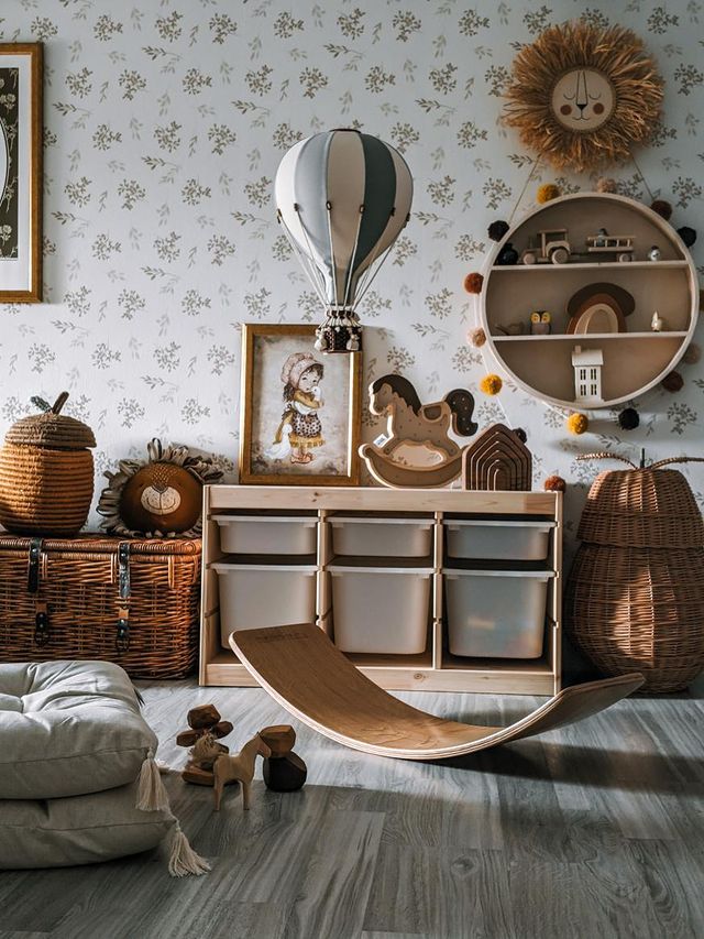 A cozy children's playroom features wooden toys, wicker baskets, and handmade decor like the Hot Air Balloon - Mint Green and Grey. A small shelf holds bins and decor; a round wall shelf displays houses and a rocking horse.