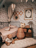 A cozy, vintage-style children’s bedroom with floral wallpaper, pink bedding on a metal bed, wicker baskets, plush toys, and a teddy bear features soft lighting and charming décor like the Hot Air Balloon - Gold.