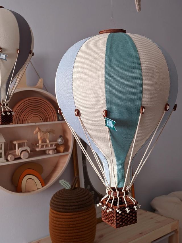 A fabric Hot Air Balloon - Mint Green and Grey hangs in a nursery, with wooden shelves behind it displaying a toy horse, truck, and rainbow shapes for whimsical handmade children’s room decor.
