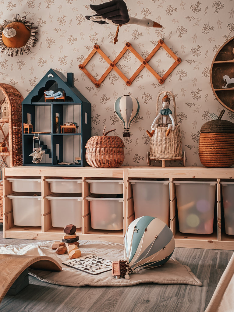 A cozy, organized children’s playroom with wooden storage bins, wicker baskets, a blue dollhouse shelf, handmade decor, toys on the floor, and a whimsical Hot Air Balloon - Mint Green and Grey. The space feels warm in neutral tones.