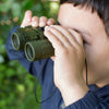 A child looks into the distance through Huckleberry Binoculars, with greenery softly blurred in the background.