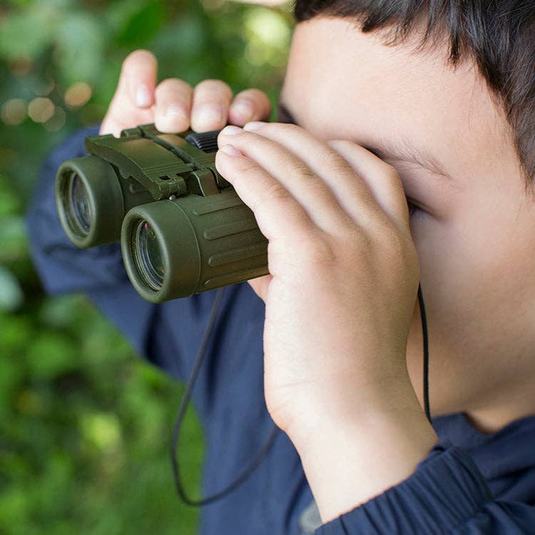 A child looks into the distance through Huckleberry Binoculars, with greenery softly blurred in the background.