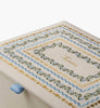 A close-up of the Delphine Large Embroidered Keepsake Box reveals decorative beige fabric adorned with blue, green, and gold wavy embroidery, featuring the word “Infant” stitched in gold at the center. A light blue ribbon peeks out on the left, making this a charming keepsake box for treasured memories.