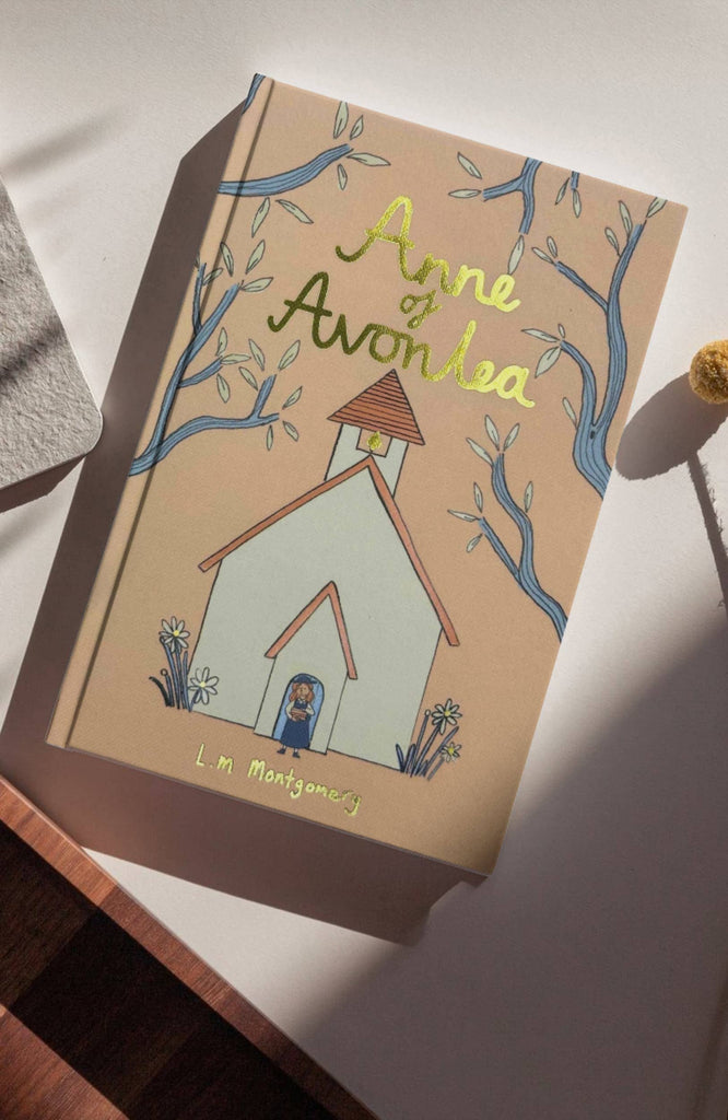 Cover of "Anne of Avonlea" Collector's Edition Hardcover by L.M. Montgomery, featuring a church surrounded by trees on a beige background, enhanced with hand-drawn text and sunlight shadows, echoing Anne's role as a teacher at her old school.