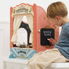 A young boy sits beside the Tabletop Puppet Wooden Theater, writing "SHOW TIME" on a chalkboard. The theater features curtains and animal puppets inside, perfect for imaginative play and creative storytelling.