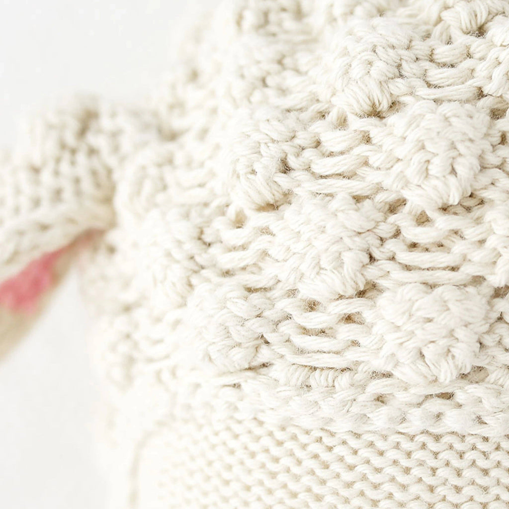 Close-up of Cuddle + Kind Benjamin the Lamb, featuring cream-colored, textured, hand-knit 100% cotton fabric with a hint of soft pink. Handmade in Peru.