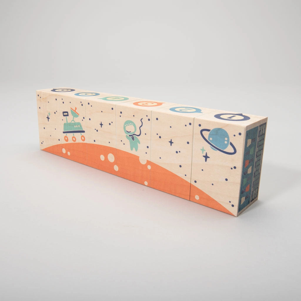 A Uncle Goose Environments Space Blocks decorated with colorful outer space-themed illustrations, including a rocket ship, planets, and stars, on a light grey background.