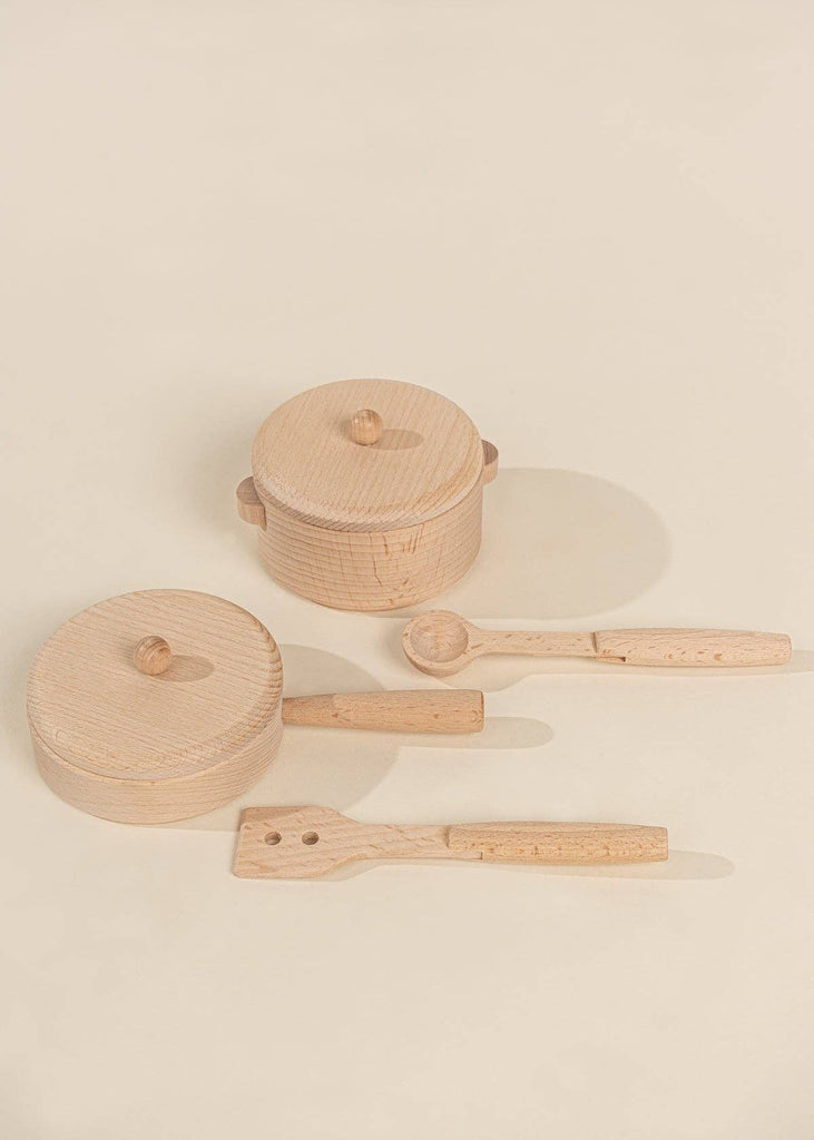 The Wooden Pots and Pans Playset (6 Pcs), featuring two wooden toy pots with lids, a wooden spoon, and a wooden spatula arranged on a light beige surface, makes the perfect addition to any wooden play kitchen or kids cooking set.