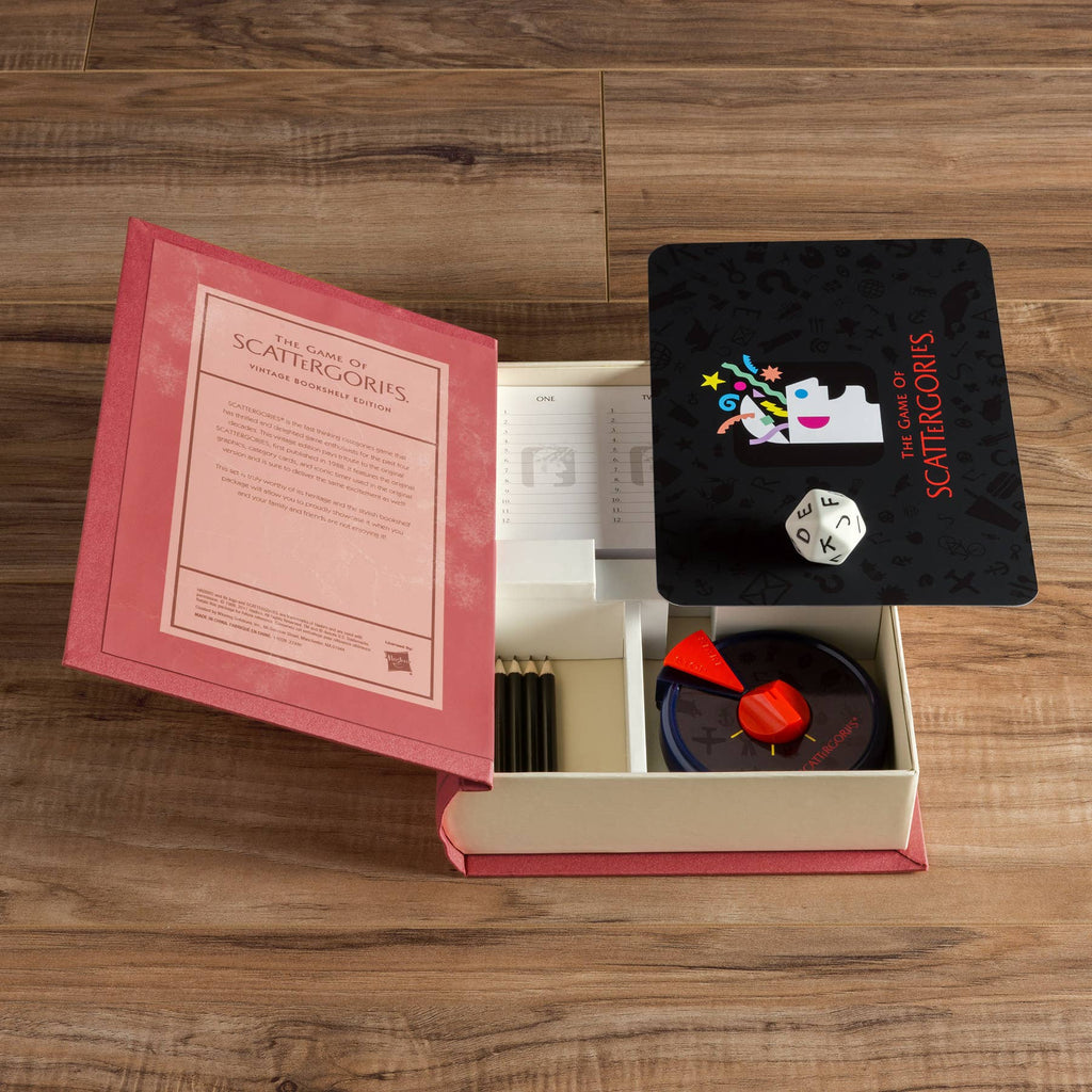 An open Board Game: Scattergories Vintage Bookshelf Edition box on a wooden floor displays the rulebook, answer pads, pencils, timer, die, and category cards neatly inside—echoing the classic 1988 version.
