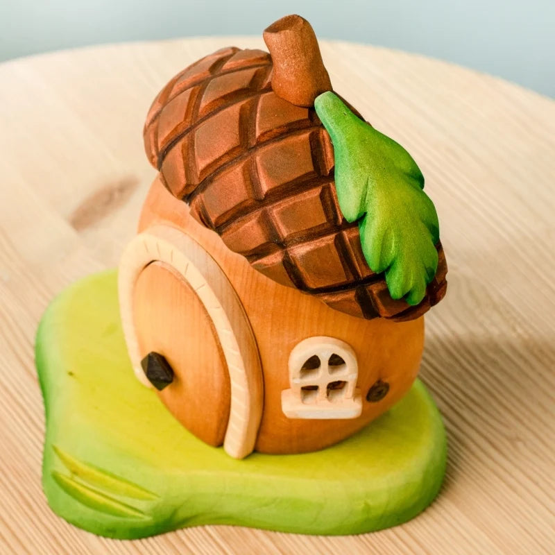 The Bumbu Handmade Wooden Acorn House features a brown textured roof, green leaf detail, round door, and tiny window on a green base—perfect as a Montessori Waldorf toy or whimsical fairy dwelling.