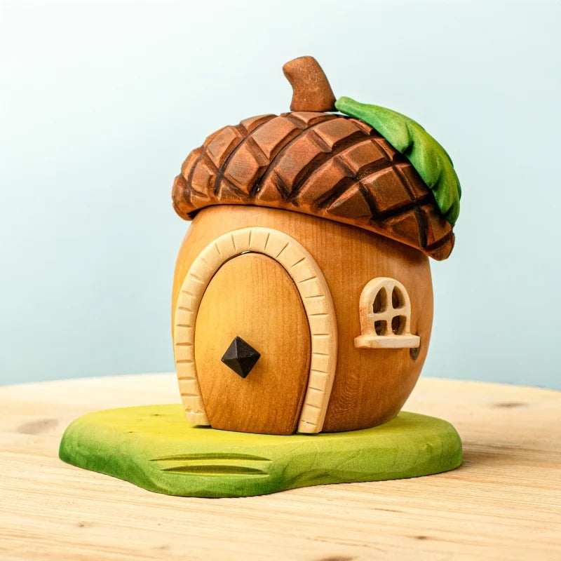 The Bumbu Handmade Wooden Acorn House is a whimsical toy shaped like an acorn, featuring a brown textured cap roof, green leaf detail, arched door, and small window—an enchanting fairy home inspired by Montessori Waldorf design.
