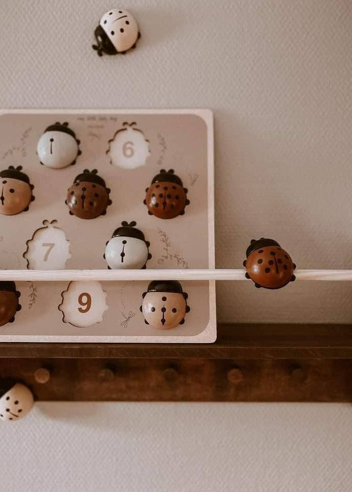 The My Little Lady Bug Wooden Puzzle, inspired by Montessori toys, features ladybug-shaped pieces in brown, white, and tan on a cream-colored background adorned with numbers and leaf designs. This charming puzzle encourages early math skills through playful hands-on learning.