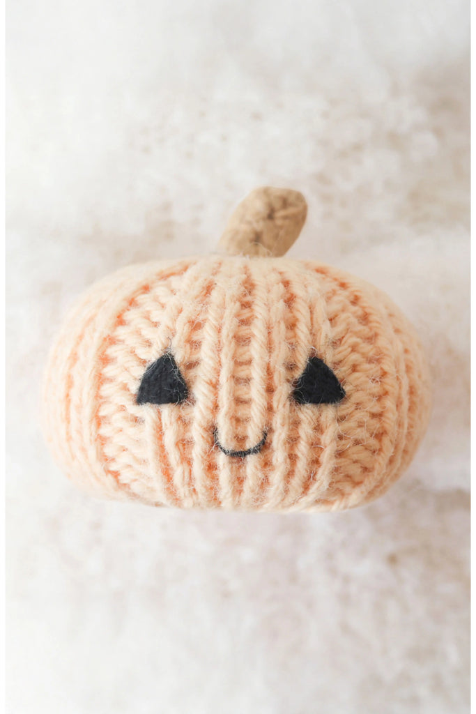 The Cuddle + Kind Baby Ghost with Pumpkin, made from soft Peruvian cotton yarn, features a smiling face and sits on a plush white surface.