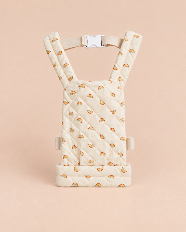 Quilted cream-colored Olli Ella Quilted Doll Carrier - Rainbow, featuring small rainbow patterns, adjustable straps, and a white plastic buckle, displayed upright on a beige background—perfectly sized as a charming doll carrier for imaginative play.