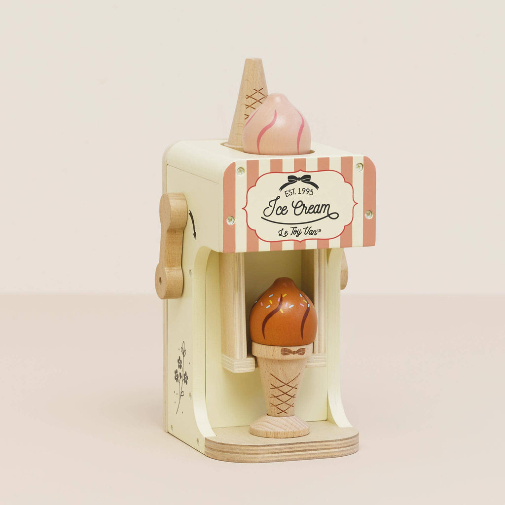 Introducing the Ice Cream Machine & Play Food Cones: a delightful wooden toy with a vintage-style design ideal for pretend play. This charming set features a side hand-crank, displays an ice cream cone with chocolate topping, and elegantly showcases "Ice Cream" on the front, inviting endless imaginative adventures.