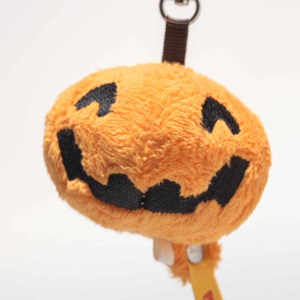 A plush keychain shaped like a jack-o’-lantern with a black stitched smile and eyes, the Steiff Little Pumpkin Keychain is a charming Halloween accessory hanging from a brown strap against a plain white background.