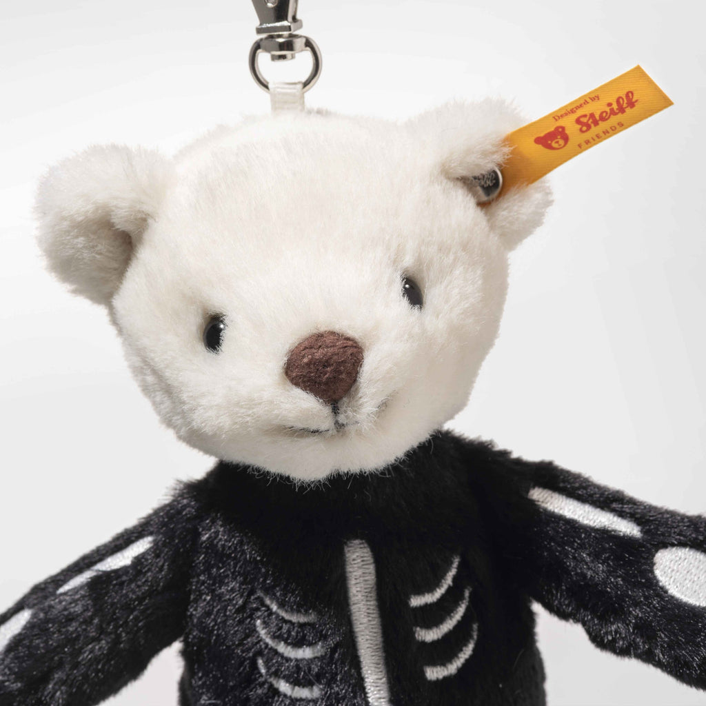 The Steiff Mr. Bones Teddy Bear Keychain features a white head, brown nose, and black body with white skeleton details. It has a yellow Steiff tag in its ear and comes attached to a silver clasp for easy use.