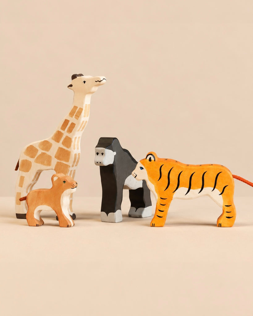 A Holztiger Handmade Wooden Safari Animals Set featuring four handcrafted wooden figures: a giraffe, a lion cub, a gorilla, and a tiger.