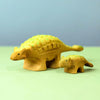 The Bumbu Handmade Wooden Ankylosaurus Dinosaur Set in yellow with green dots rests on a light green surface against a blue background—perfect as an educational toy for imaginative play.