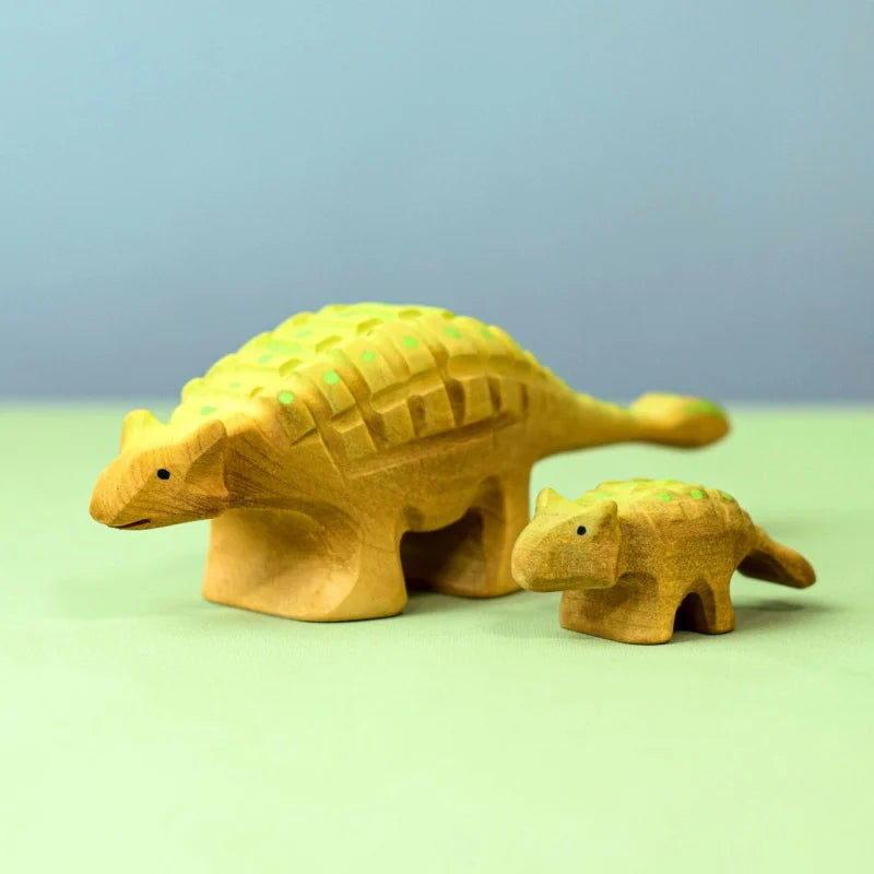 The Bumbu Handmade Wooden Ankylosaurus Dinosaur Set in yellow with green dots rests on a light green surface against a blue background—perfect as an educational toy for imaginative play.