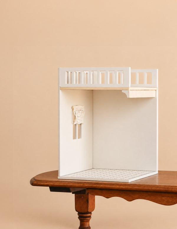 A minimalist white dollhouse room with a balcony and tiled floor sits on a wooden table against a beige background, providing the perfect setting for the Maileg House of Miniature Bonus Room - Bathroom or inspiring imaginative play as an additional bonus room.