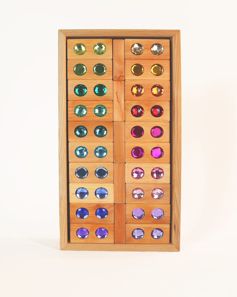 Wooden tray filled with two columns of Bauspiel Large Gem Blocks, 45-Piece Set, each featuring a colorful, faceted plastic gem in the center.