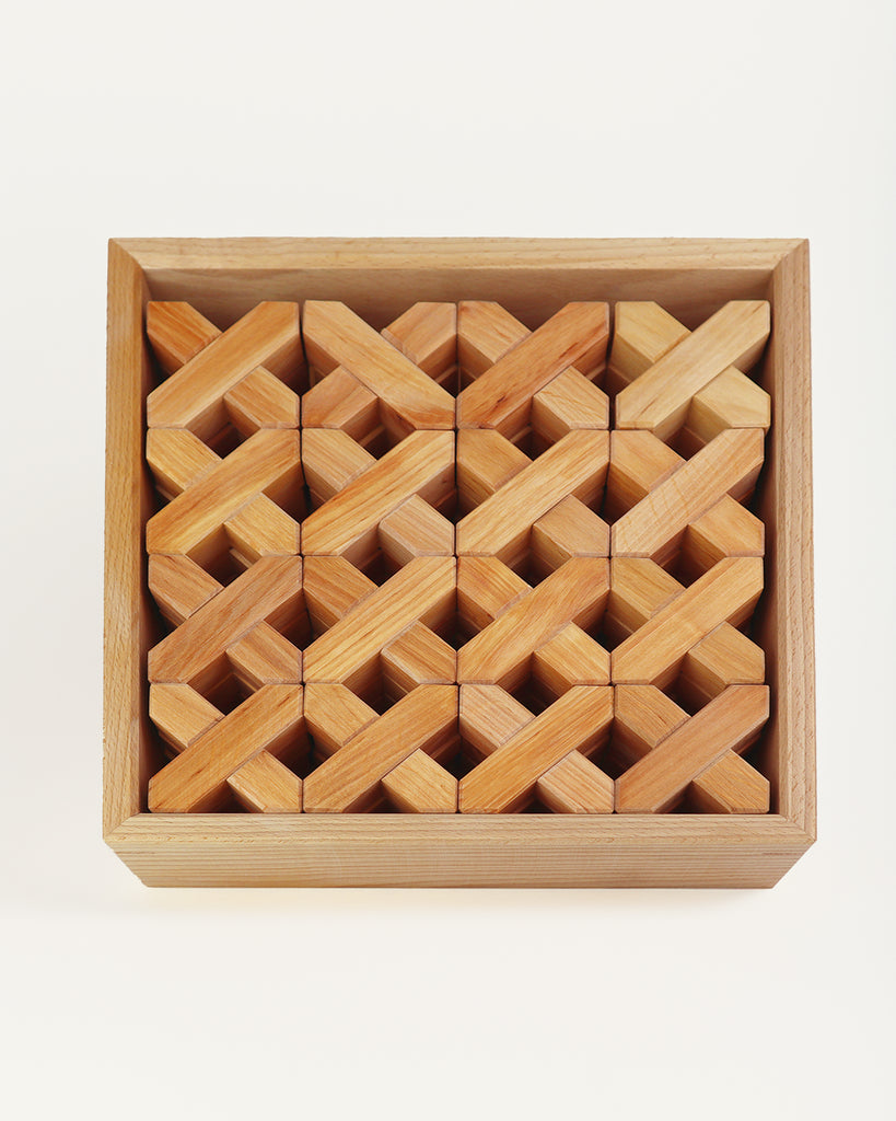 A wooden tray filled with 48 Bauspiel X-Blocks, 48-Piece Set in Wooden Tray arranged in a grid of interlocking X-shaped patterns.
