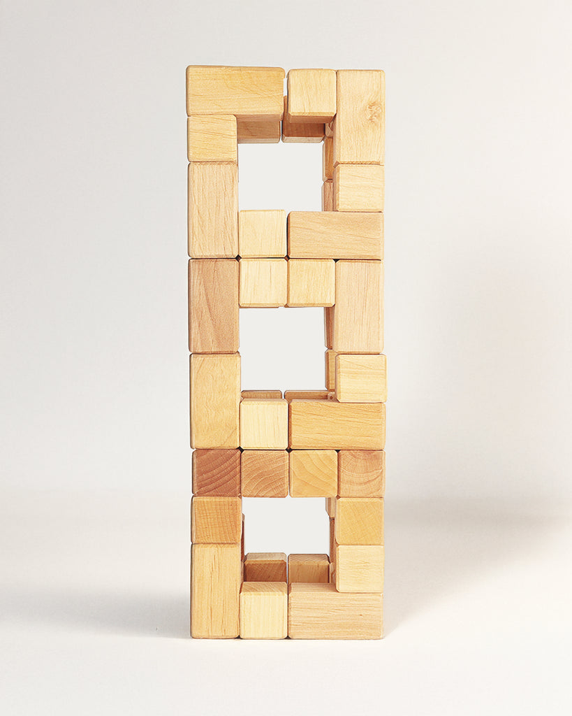 A tall, rectangular tower built from twenty-four light-colored Bauspiel Natural Corner Blocks with three open square spaces in the center.