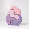 Grimm's Casa Coral Building Blocks is a handpainted wooden puzzle with five pastel-colored, interlocking pieces in pink, lavender, and purple that form an abstract shape—ideal as toddler toys or building blocks on a plain white background.