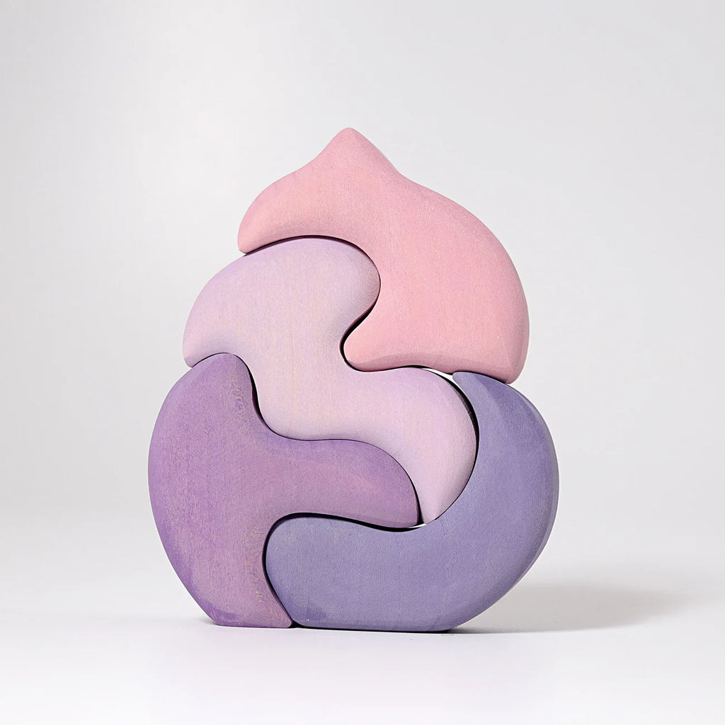 Grimm's Casa Coral Building Blocks is a handpainted wooden puzzle with five pastel-colored, interlocking pieces in pink, lavender, and purple that form an abstract shape—ideal as toddler toys or building blocks on a plain white background.