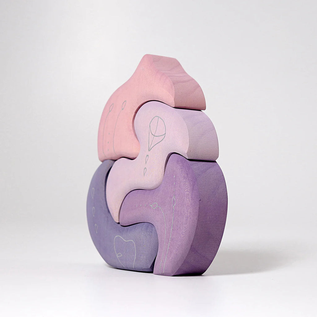 Grimm's Casa Coral Building Blocks features four handpainted wooden puzzle pieces in pastel pink and purple, stacked vertically to form an abstract, curved shape with delicate white line drawings, displayed on a plain white background.