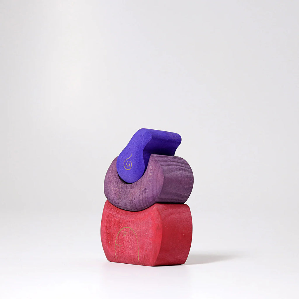 Grimm's Small Bakery Building Blocks—three colorful, curved wooden pieces in red, purple, and blue—are stacked on a white surface against a plain background, sparking imaginative play.