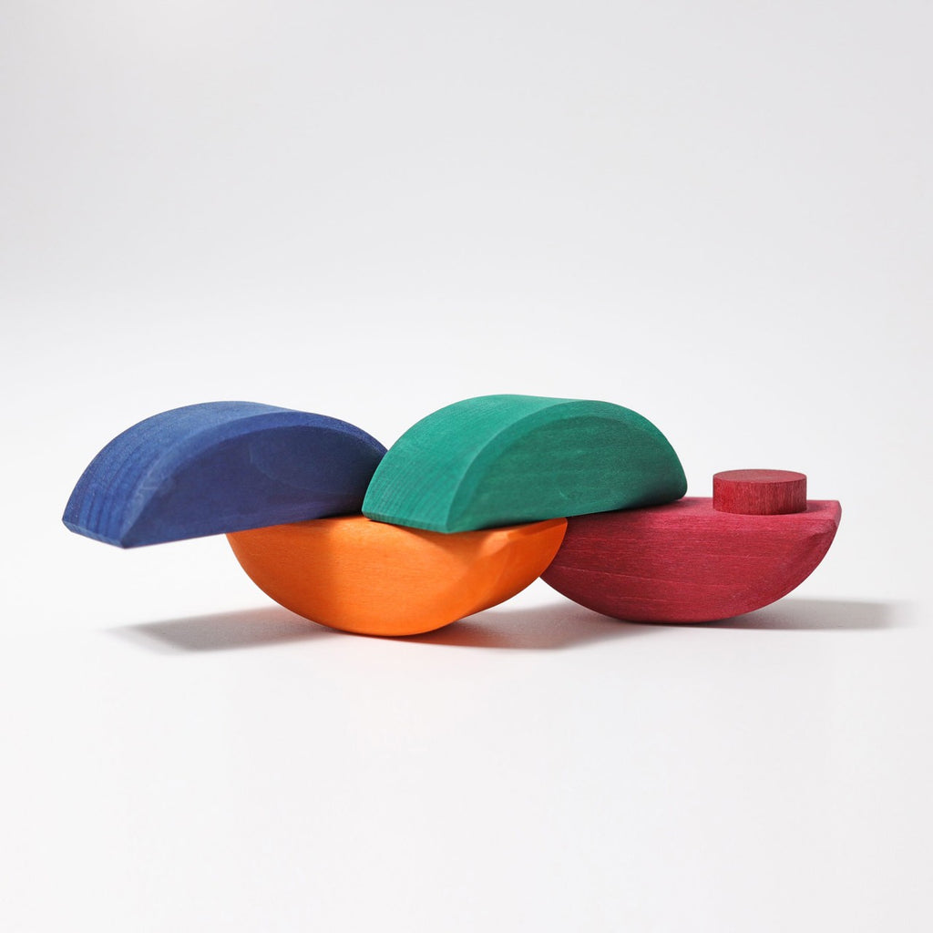 The Grimm's Rolling Boats balancing toys come in vibrant colors—blue, green, orange, and red—and are stacked on top of each other against a plain white background. Each non-toxic piece, perfect for small children, features curved shapes with some flat sides or small cylindrical attachments. The set includes 12 pieces overall.