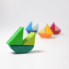 Grimm's Rolling Boats, crafted from non-toxic wood, are arranged in a diagonal line against a white background. The nearest boat is a bright green with a teal base, while the other boats fade into the background with vibrant colors such as blue, yellow, orange, and red—ideal for small children.