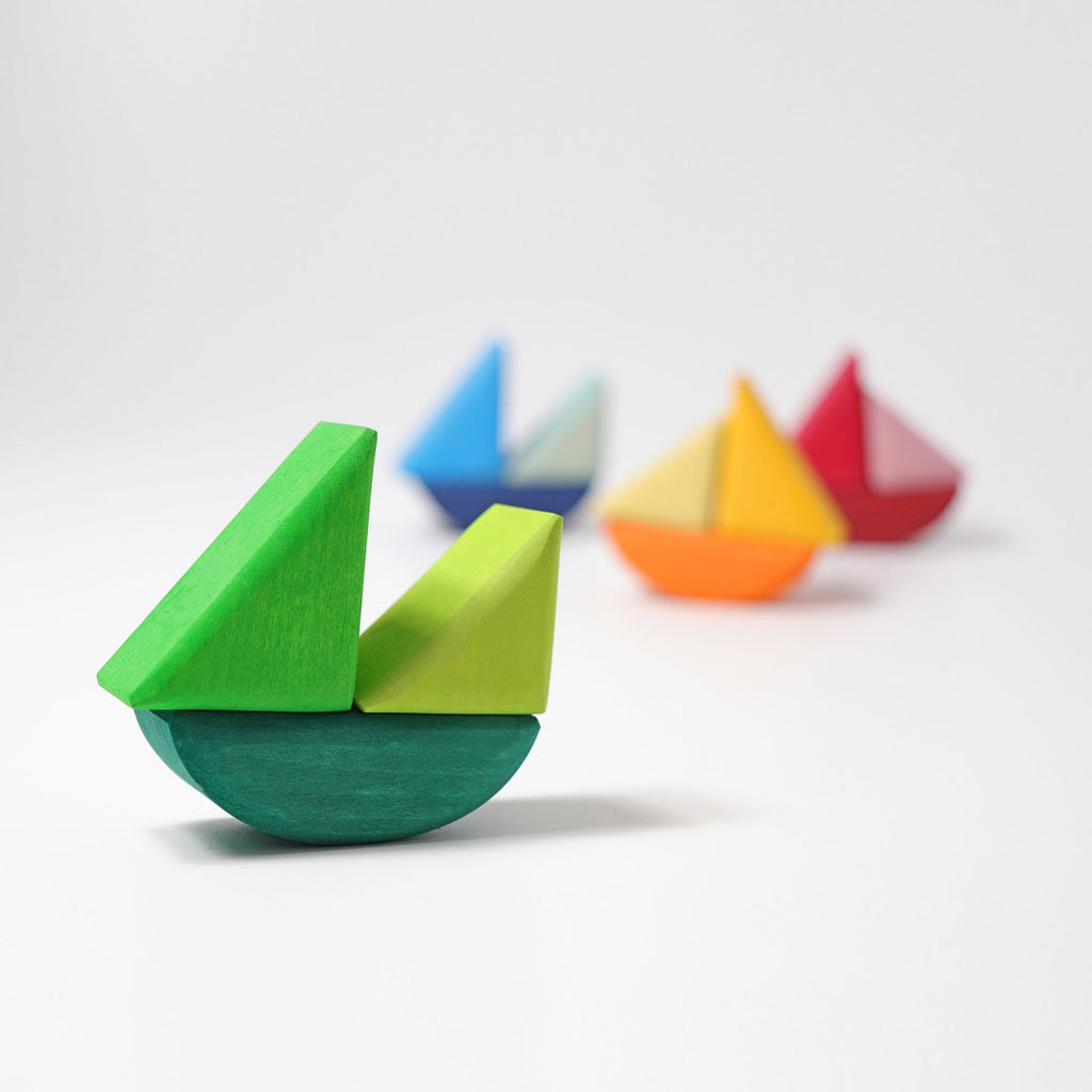 Grimm's Rolling Boats, crafted from non-toxic wood, are arranged in a diagonal line against a white background. The nearest boat is a bright green with a teal base, while the other boats fade into the background with vibrant colors such as blue, yellow, orange, and red—ideal for small children.