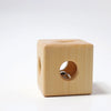 The Grimm’s Cube with Bell (ships in 2-3 weeks), a lightweight and compact wooden toy featuring smooth edges and circular holes on each side, rests on a white surface. Through one of the openings, a metal bell can be seen inside the cube, making this a delightful non-toxic baby toy.