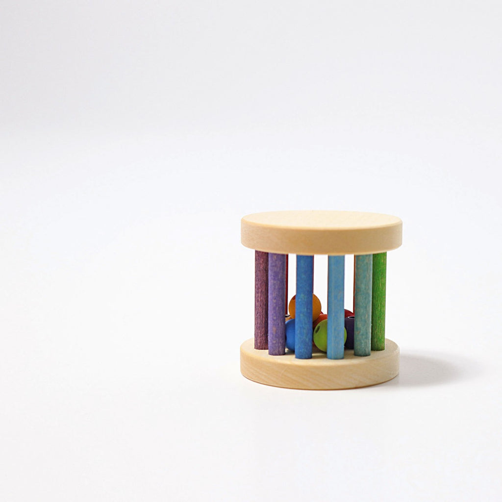 A Mini Rolling Wheel lies on a plain white surface, featuring a cylindrical shape with multicolored vertical bars and small colorful balls enclosed inside. The top and bottom are circular wooden caps, and within, tiny wooden beads create sound as they move around like a colorful wheel.