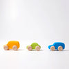 Three small Grimm's Colored Wooden Cars in yellow, green, and blue are lined up on a white surface. Each non-toxic car features natural wood wheels and a simple design against a plain white background.