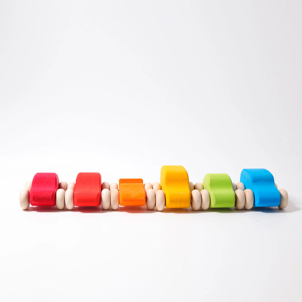 Six Grimm's Colored Wooden Cars in red, orange, yellow, green, and blue are lined up against a white background. Each non-toxic car features white wheels and a smooth, minimalist design for safe play.